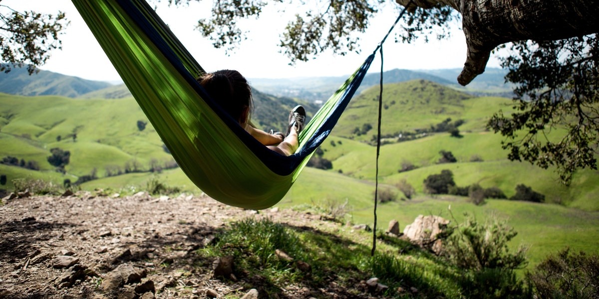 Person relaxing in a green hammock, enjoying panoramic view of rolling hills and nature.