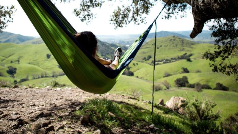 Person relaxing on a hammock with a scenic view of rolling green hills and clear blue sky.