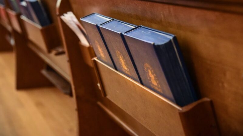 Hymnals in a wooden pew slot at a church, highlighting religious service preparation and seating arrangement.