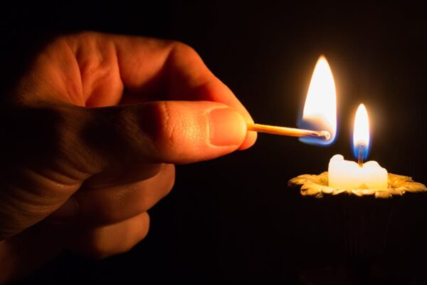 Hand lighting a candle with a matchstick in dark background, creating a warm glow.