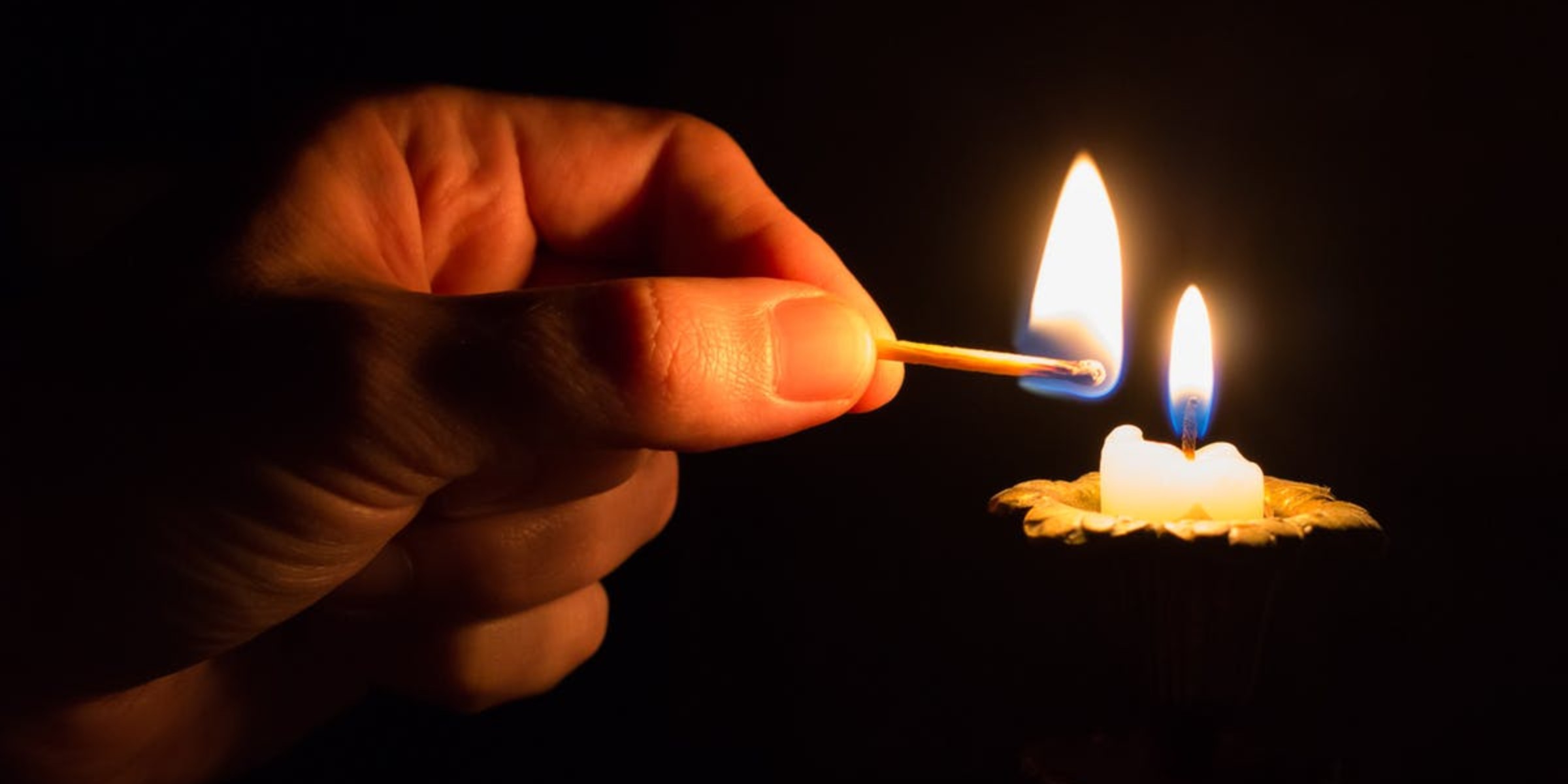 Hand lighting a candle with a matchstick in dark background, creating a warm glow.