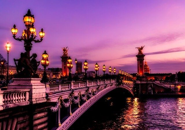 Elegant bridge in Paris at sunset with glowing streetlights and a vibrant purple sky.