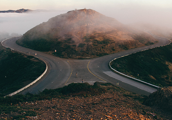 Mountain road at fork with misty hill in background, serene landscape.