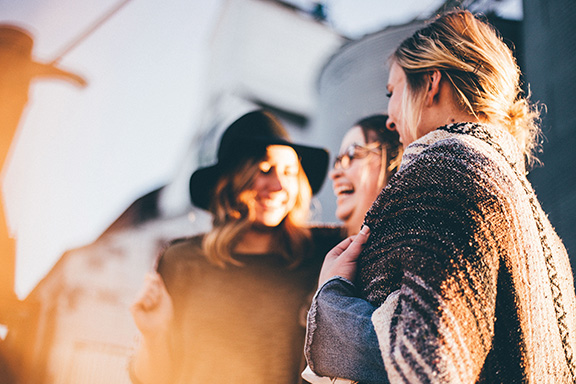 Group of friends laughing and enjoying a sunny day outside, wearing casual clothing and hats.