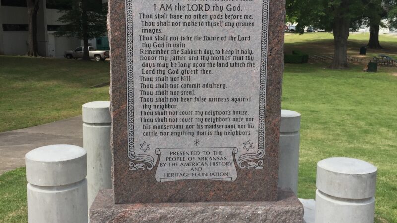 Granite Ten Commandments monument in a park setting with green trees in the background.