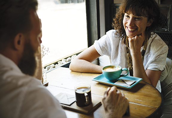 Woman smiling at a man over coffee in a cozy cafe setting.