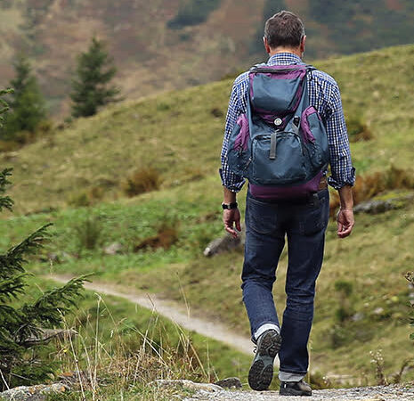 Man hiking on a mountain trail with a backpack, surrounded by lush greenery and trees.