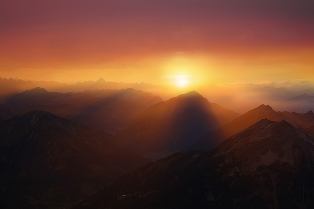 Stunning sunset over mountain range with vibrant orange sky, highlighting silhouetted peaks and tranquil atmosphere.