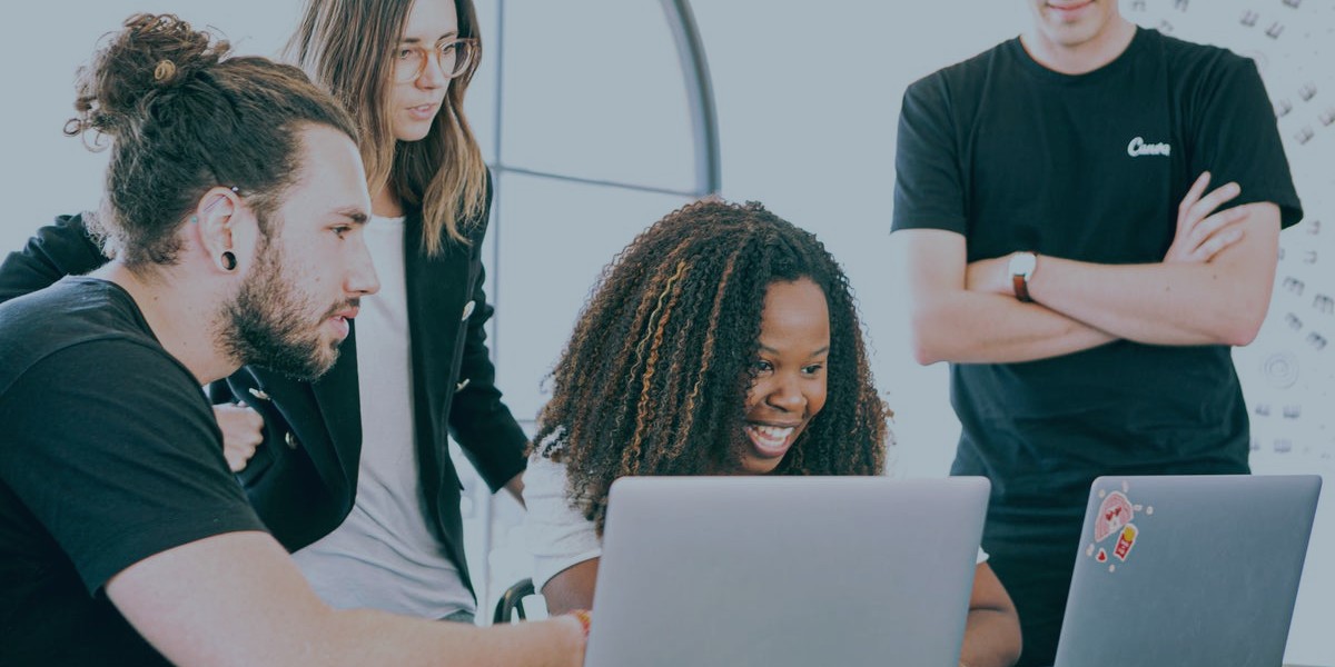 Group of diverse colleagues collaborating on laptops with smiles in a bright office space.