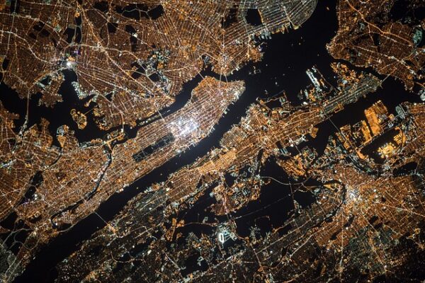 Aerial night view of illuminated city grid and waterways, showcasing urban landscape and infrastructure from above.