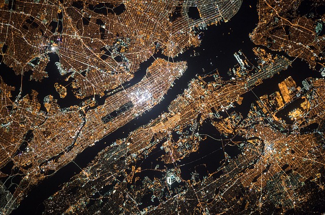 Aerial night view of illuminated city grid and waterways, showcasing urban landscape and infrastructure from above.
