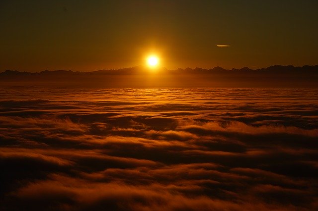 Sunrise over a sea of clouds with a warm glow, creating a serene and majestic skyscape.