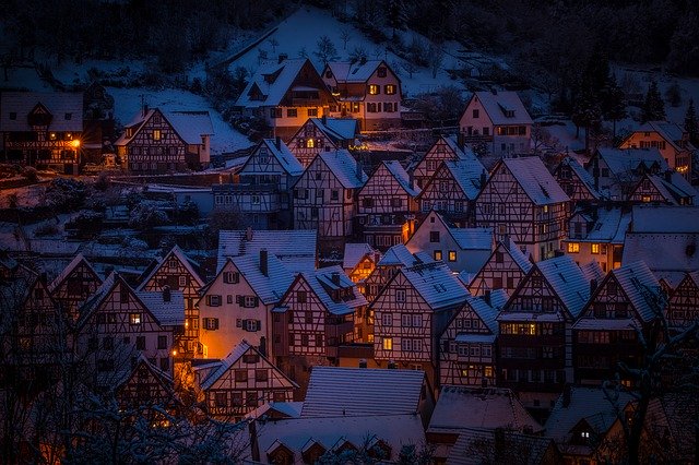 Snow-covered village at dusk with warm glowing lights, showcasing winter charm and traditional architecture.