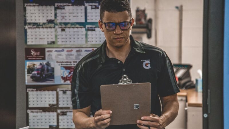 Man reading clipboard in office with wall calendars in background.