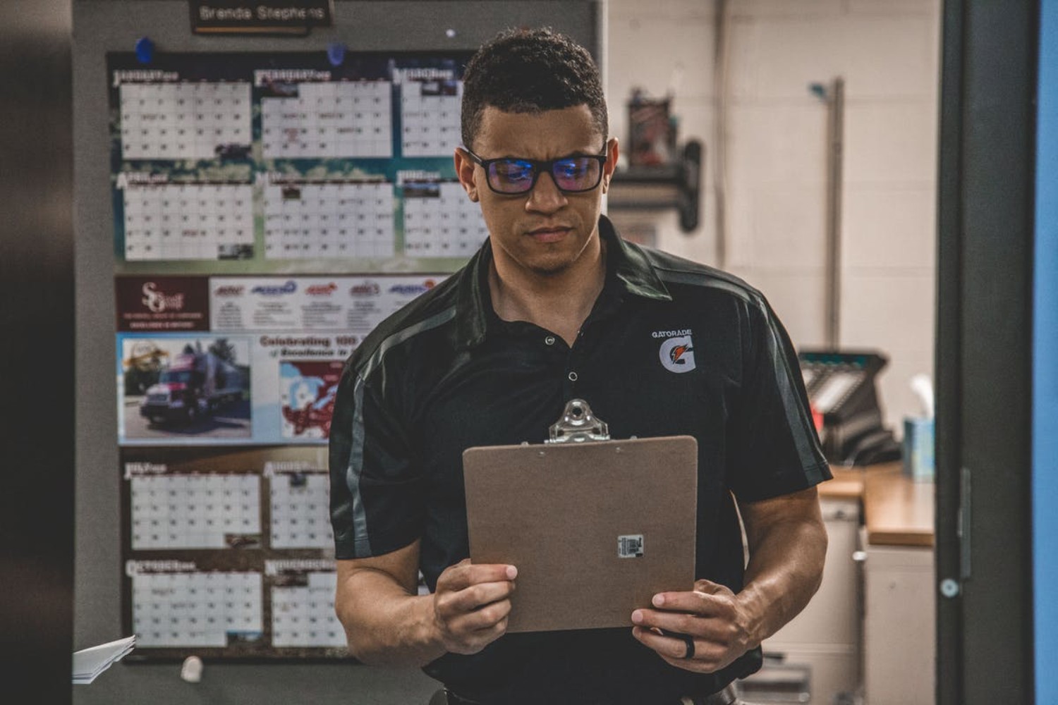 Man reading clipboard in office with wall calendars in background.