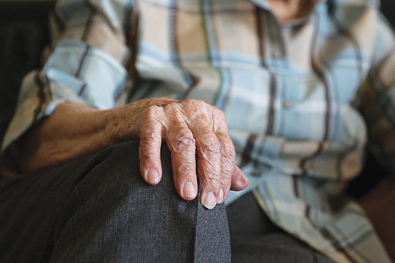 Elderly hand resting on knee, wearing checkered shirt, symbolizing wisdom and experience.