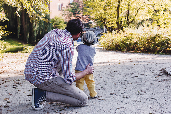 Father and child walking in a sunny park, father in plaid shirt and child in hat.