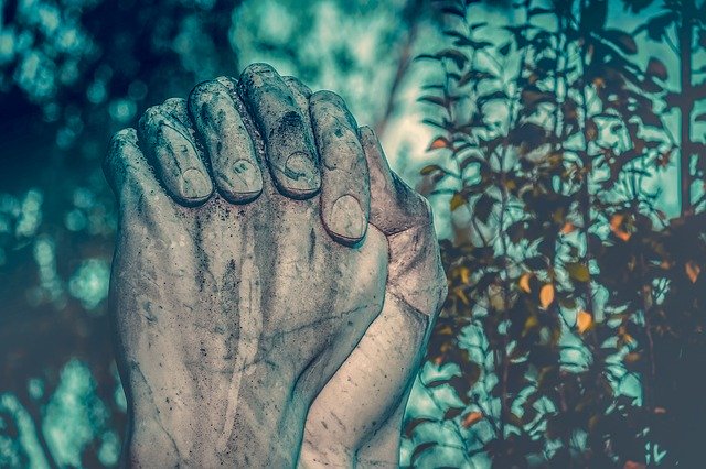 Close-up of two intertwined hands statue with a natural background, symbolizing unity and support.