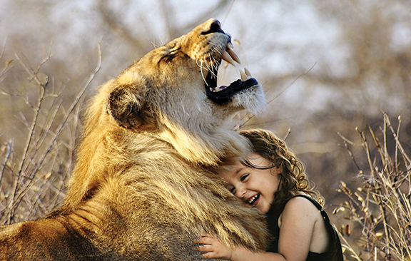 A joyful child embraces a relaxed lion, showcasing a unique bond in a natural setting.