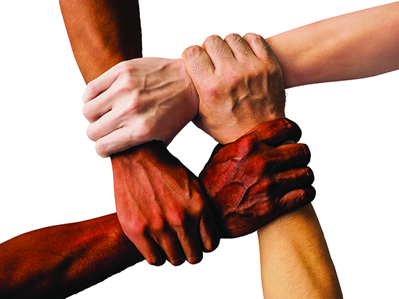 Four hands of diverse skin tones interlocked, symbolizing unity and teamwork on a white background.