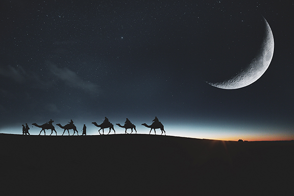 Camel caravan traveling under a crescent moon and starry night sky in the desert landscape.
