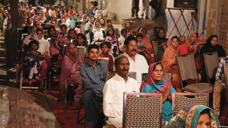 A diverse community gathering in an outdoor setting, seated attentively and engaged in an event.