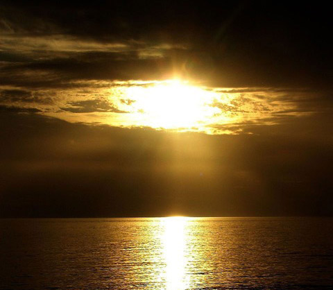 Golden sunset over the ocean with dramatic clouds and reflective water.