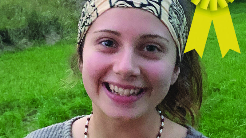 Smiling person wearing a headband with a third-place ribbon in a grassy outdoor setting.