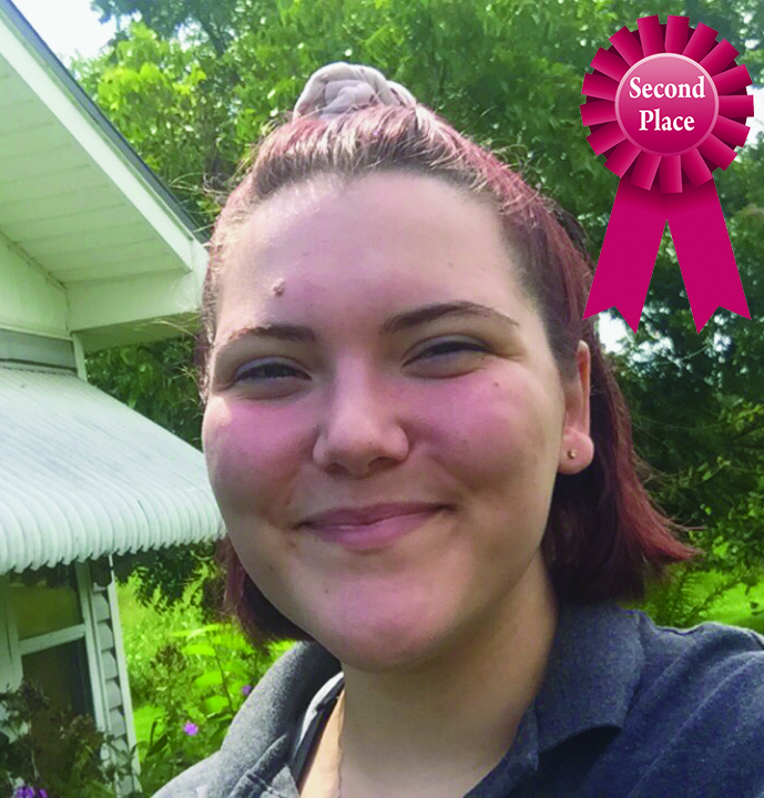 Smiling person outdoors with a second-place ribbon in the corner, green garden background.
