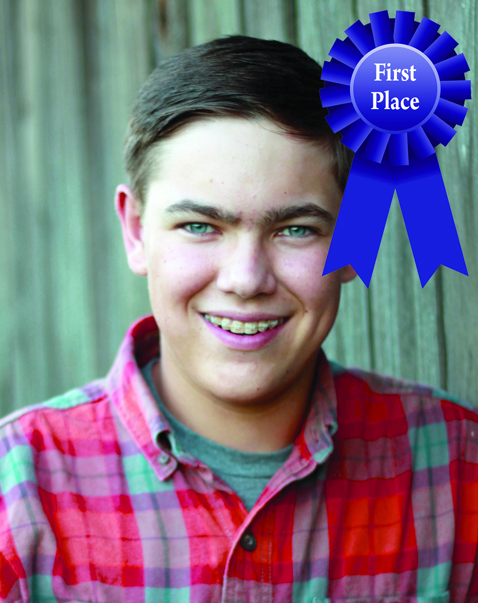 Smiling boy with braces wearing a plaid shirt, awarded a blue first-place ribbon.