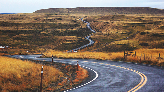 Winding road through hilly grasslands under a cloudy sky, perfect for road trip adventure and nature exploration.