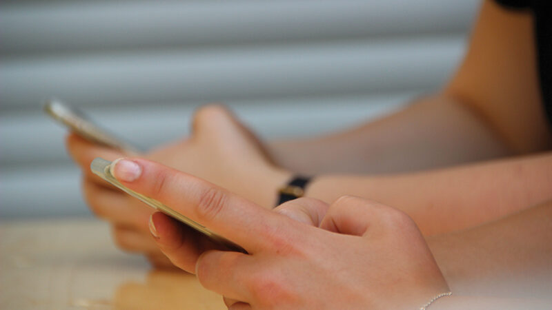 Two people using smartphones, focusing on hands and devices, in a casual setting.