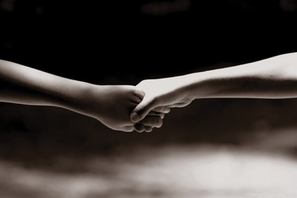 Two hands holding each other, symbolizing connection and support, against a dark background.