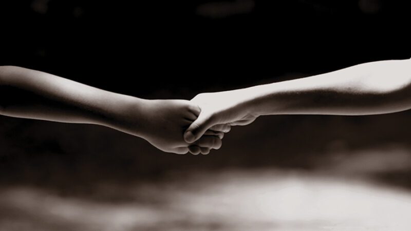Two hands holding each other, symbolizing connection and support, against a dark background.