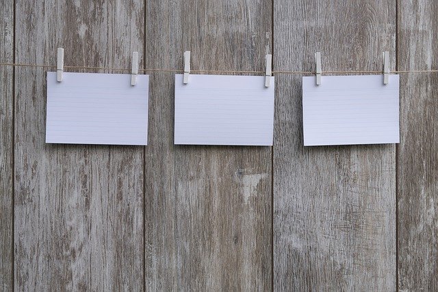 Three blank notes hanging on a clothesline against a rustic wooden background.