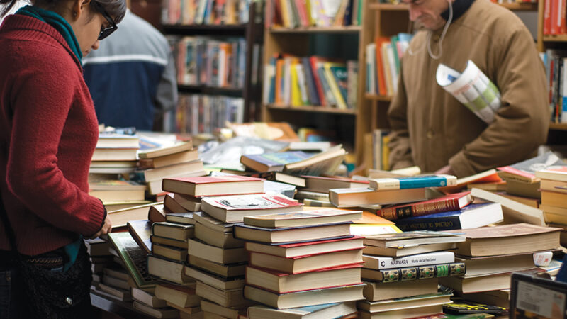 People browsing books in a cozy, vibrant bookstore, with stacks of colorful novels on the table.