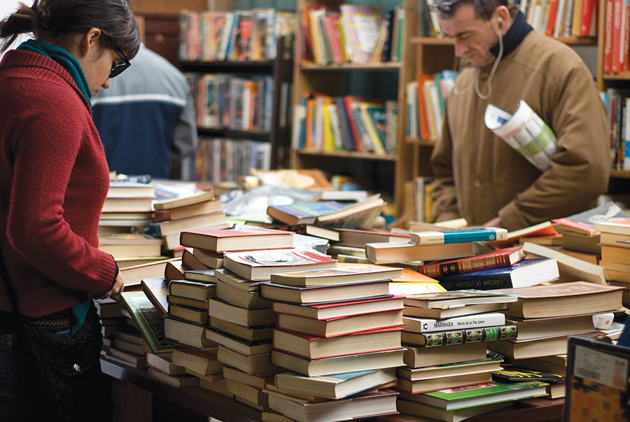 People browsing books in a cozy, vibrant bookstore, with stacks of colorful novels on the table.
