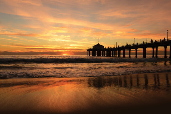 Sunset over a scenic pier with reflections on the ocean waves, creating a tranquil and vibrant atmosphere.