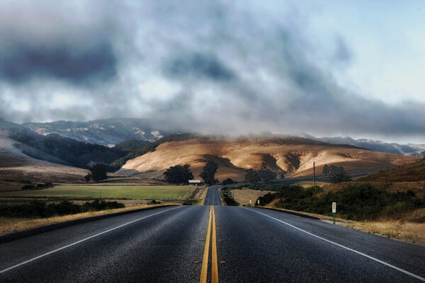Open road leading to misty hills under cloudy sky, perfect for adventure travel and serene road trip moments.