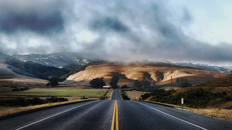 Open road leading to misty hills under cloudy sky, perfect for adventure travel and serene road trip moments.