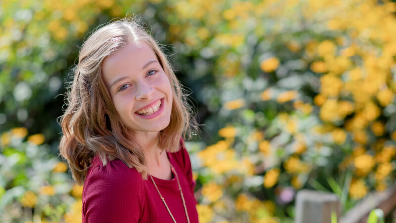Smiling woman in red dress with yellow flowers in the background.