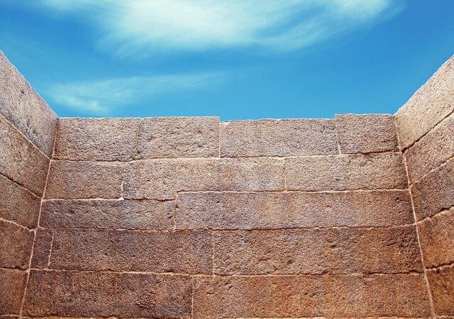 Ancient stone wall against blue sky with scattered clouds, showcasing historical architecture and clear weather.