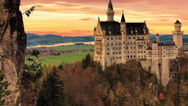 Majestic castle at sunrise, surrounded by forested hills and colorful sky, ideal for travel and architecture themes.