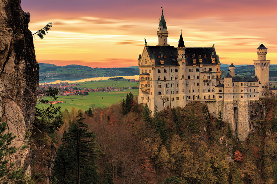 Majestic castle at sunrise, surrounded by forested hills and colorful sky, ideal for travel and architecture themes.