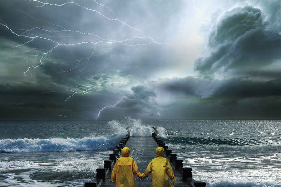 Two people in yellow raincoats hold hands on a pier during a dramatic lightning storm over the ocean.