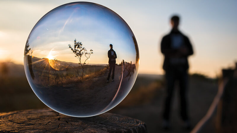 A crystal ball captures a sunset landscape with a silhouetted person in the background.