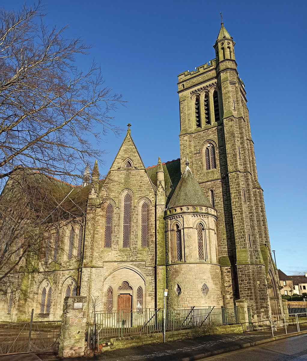 Historic stone church with tall bell tower under blue sky, surrounded by bare winter trees.