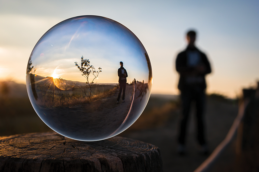 Crystal ball reflects sunset landscape and figure on a stump, with silhouette in the background.