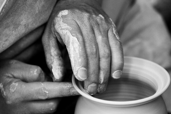 Hands shaping clay on a pottery wheel, showcasing creativity and craftsmanship in ceramics. Black and white close-up.