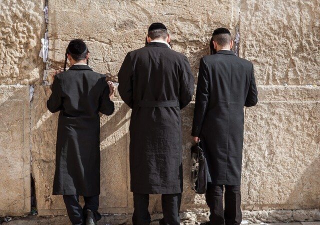 Men praying at the Wailing Wall in Jerusalem, wearing traditional black clothing and hats.